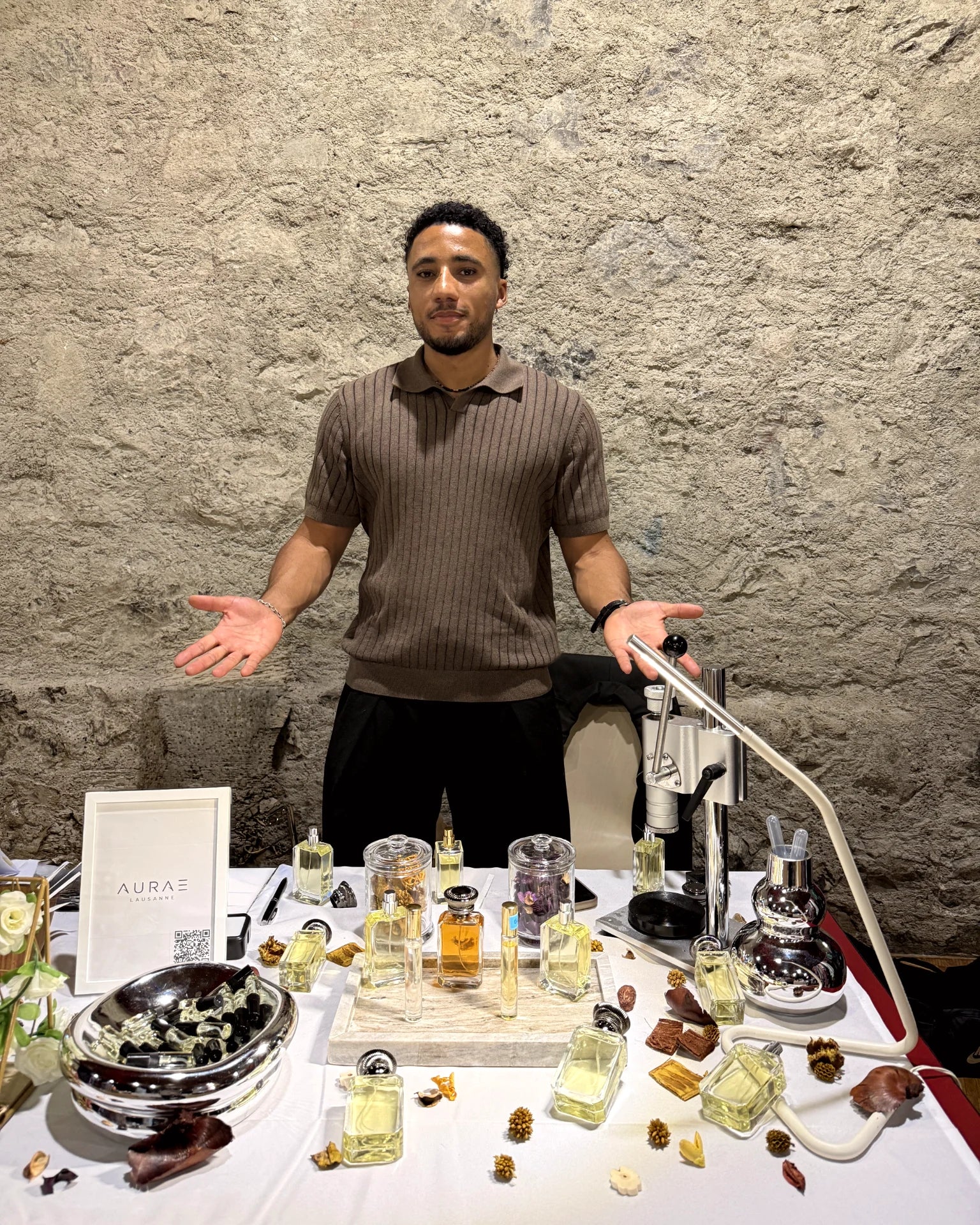 Arthur derrière le stand AURAE, avec des flacons et des échantillons de parfums.